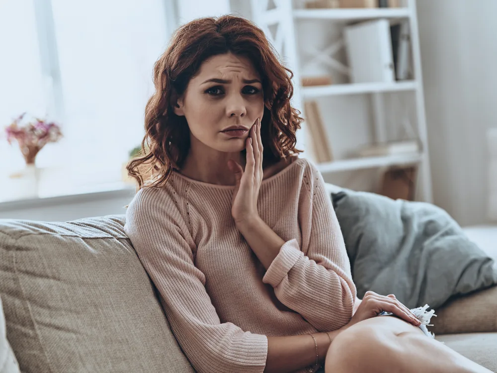A woman on a sofa holding her cheek with a toothache